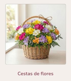 Cestas de flores personalizadas. Cesta de mimbre con flores de fressia en diferentes colores. La cesta de flores está colocada encima de una mesa clara de madera.